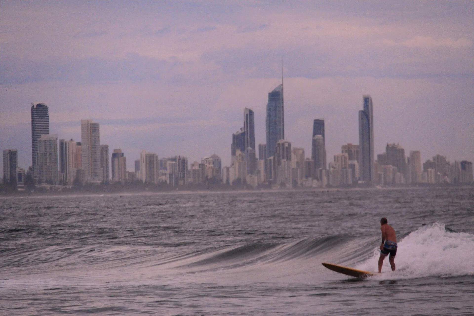 A surfer riding a wave with the Surfers Paradise skyline behind on the Gold Coast, Australia