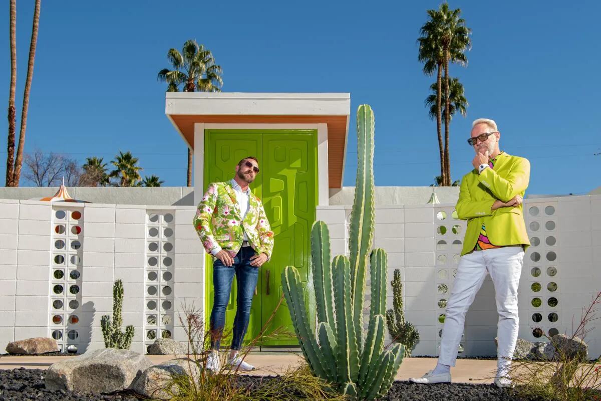 Two stylishly dressed men in bright blazers outside a lime-green mid-century door and white breeze-block wall with palms in Palm Springs, California