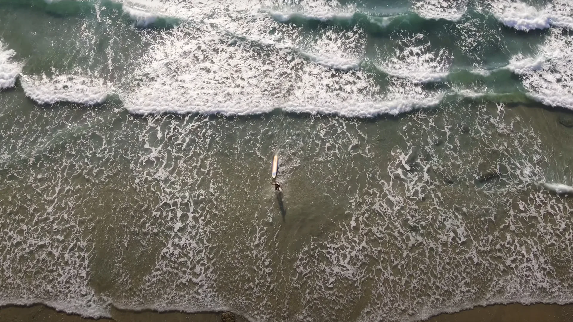 Aerial view of a surfer walking into the ocean surf at La Jolla in San Diego, California