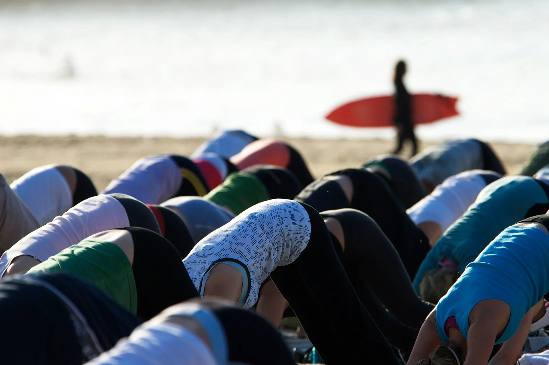 People practising yoga at dawn on the sand as a surfer walks past at Bondi Beach in Sydney, Australia