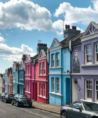 A row of brightly painted terraced houses in pink, blue and purple in Brighton, England, under a blue sky