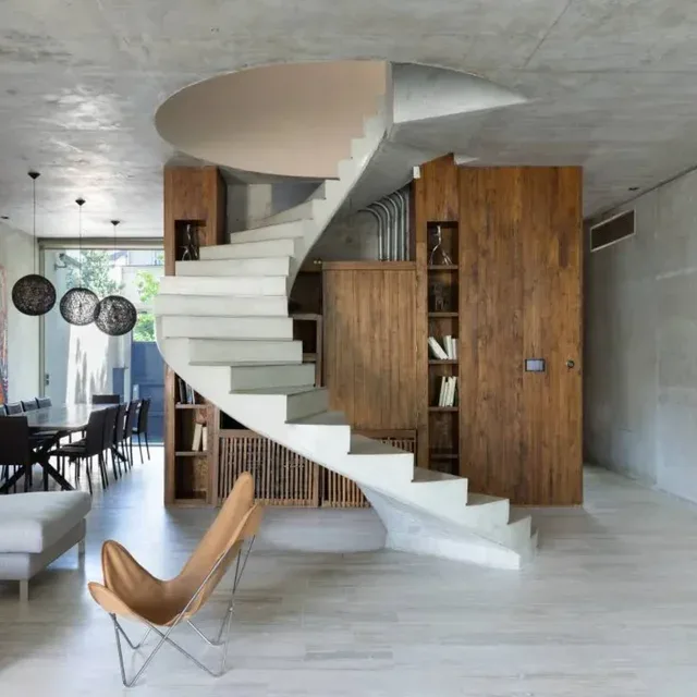 Buenos Aires home interior with a sculptural concrete spiral staircase, wood joinery and an Argentine leather butterfly chair