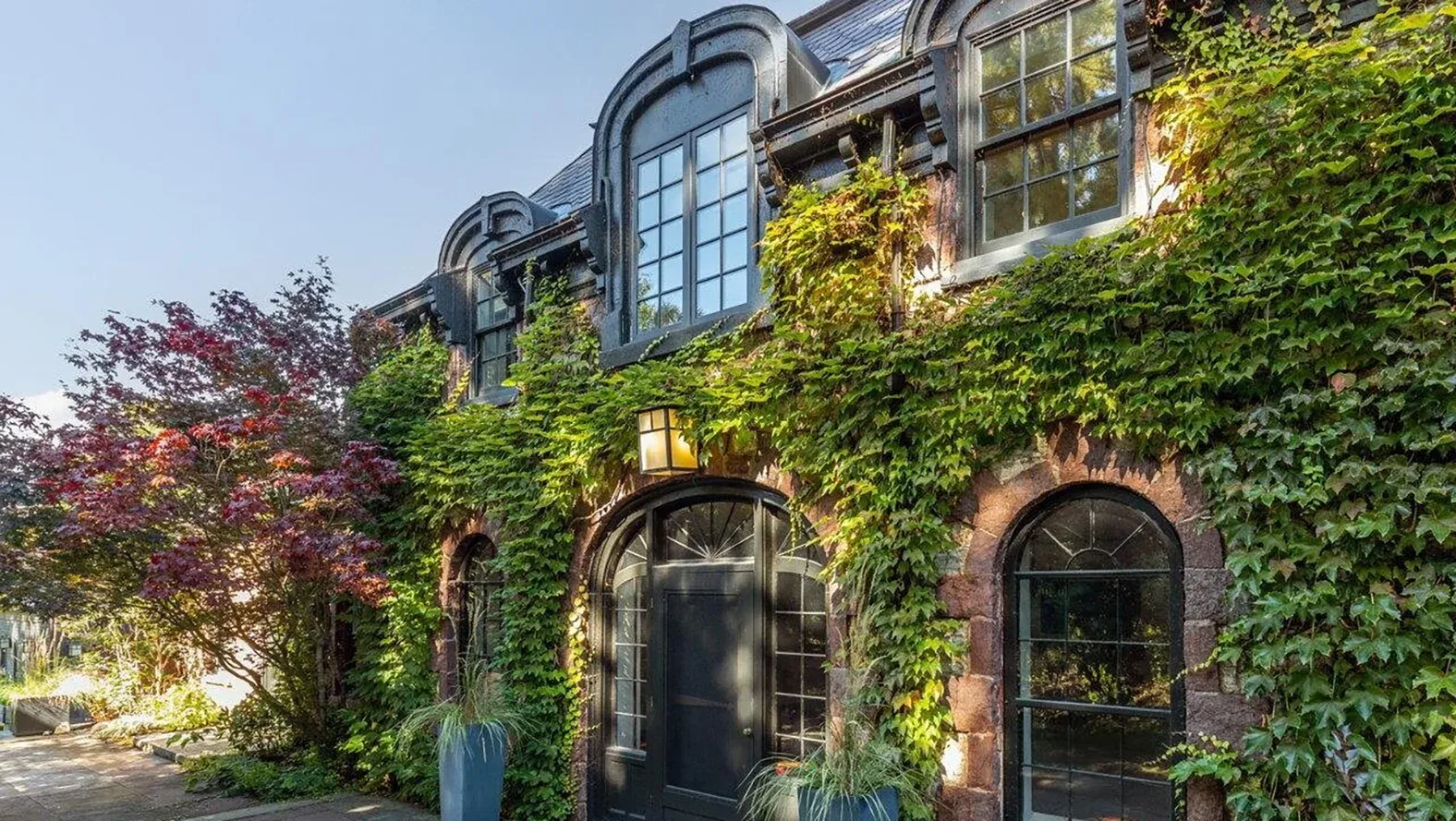 Ivy-covered historic stone home in Burlington, Vermont, with an arched black entry door, arched windows and a red Japanese maple in the front garden