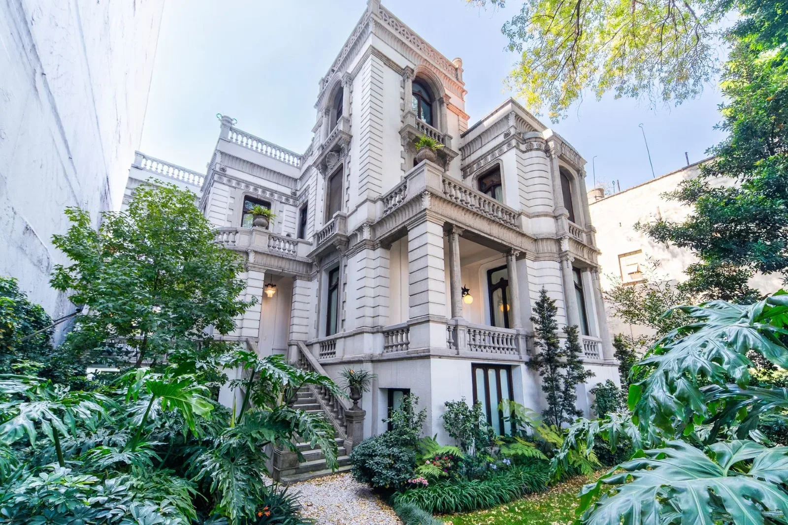 An ornate Porfirian-era stone mansion surrounded by a lush green garden in central Mexico City