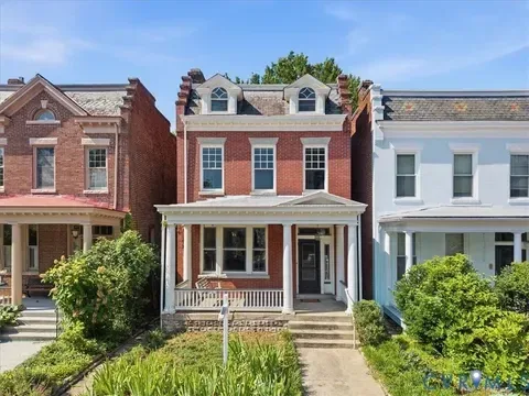 A classic three-story brick row house with a front porch on a leafy street in Richmond, Virginia