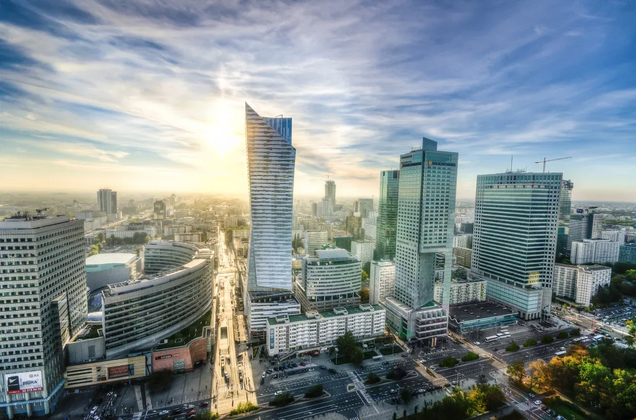Golden-hour aerial view of Warsaw's modern downtown skyline with glass skyscrapers and busy streets below