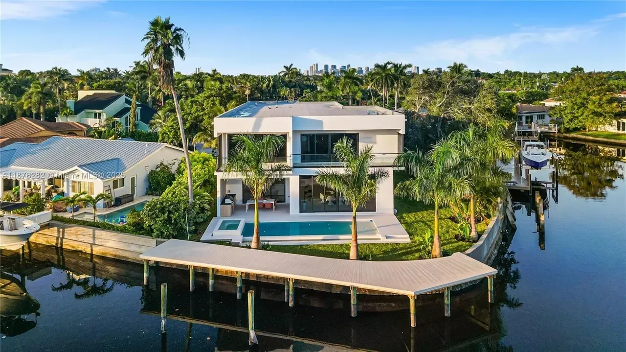 Modern white waterfront home with a pool and private dock on a canal in Wilton Manors, Florida, with the Fort Lauderdale skyline in the distance