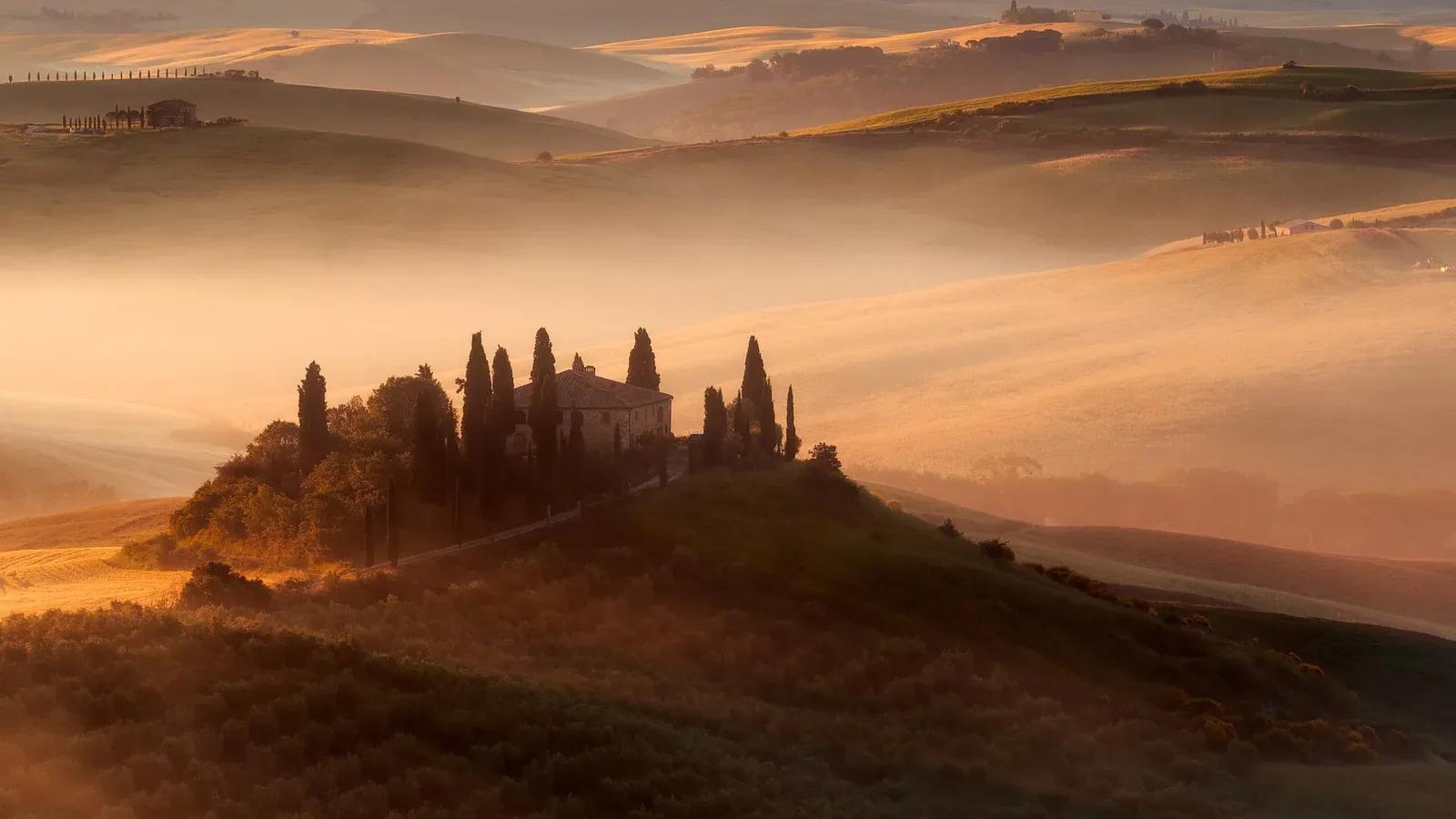 A stone Tuscan farmhouse ringed by cypress trees on a hill at golden hour in the Val d'Orcia, Italy