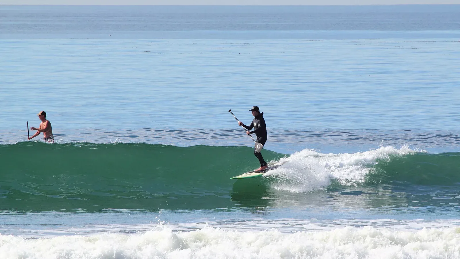 A stand-up paddle surfer riding a wave off the San Diego coast, capturing the city's active outdoor lifestyle