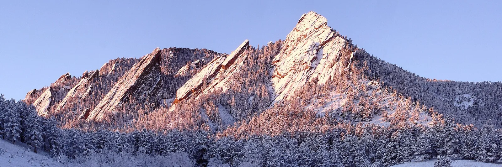 The Flatirons rock formations dusted with snow at sunrise above Boulder, Colorado