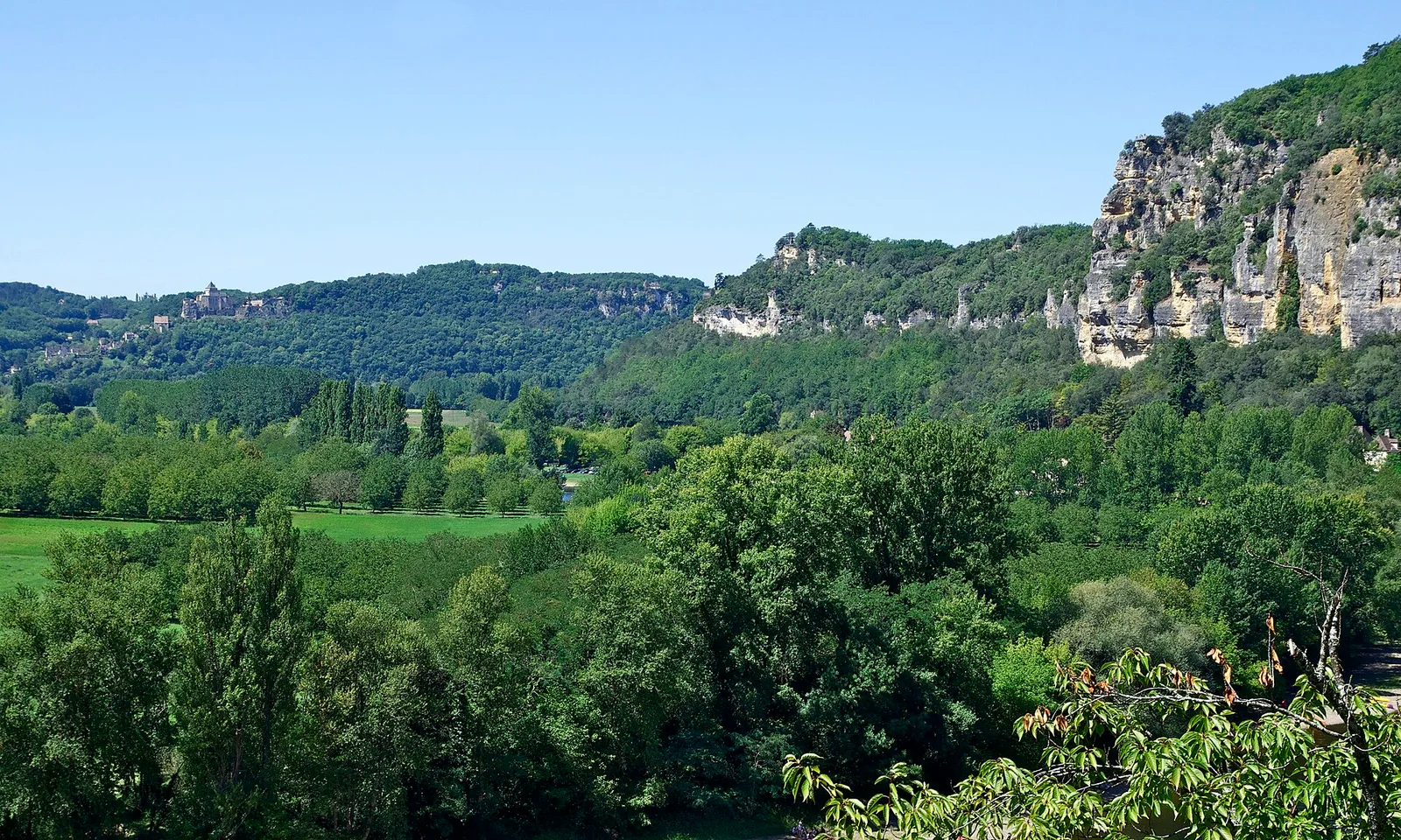 The Dordogne river winding through a green valley below limestone cliffs and a riverside village, France