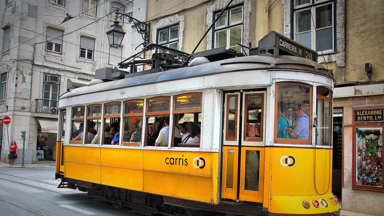 The iconic yellow Tram 28 climbing a colourful, walkable street in Lisbon, Portugal