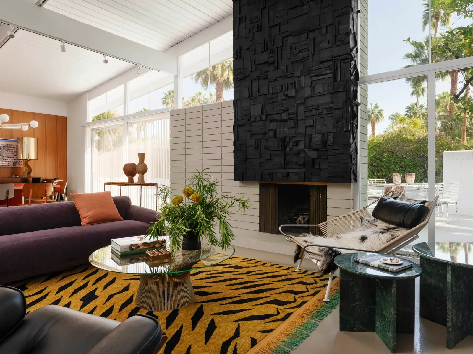 Sunlit mid-century modern living room in Palm Springs, California, with clerestory windows, a sculptural fireplace and palm trees beyond