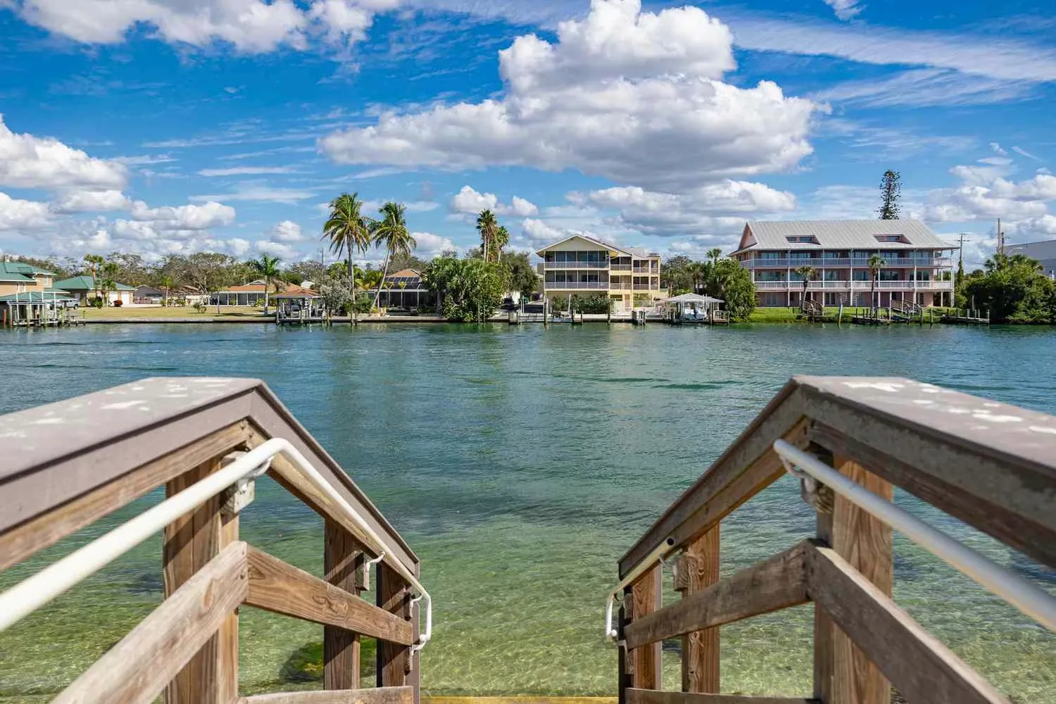 View across turquoise intracoastal water to palm-lined waterfront homes in Sarasota, Florida, from a wooden dock