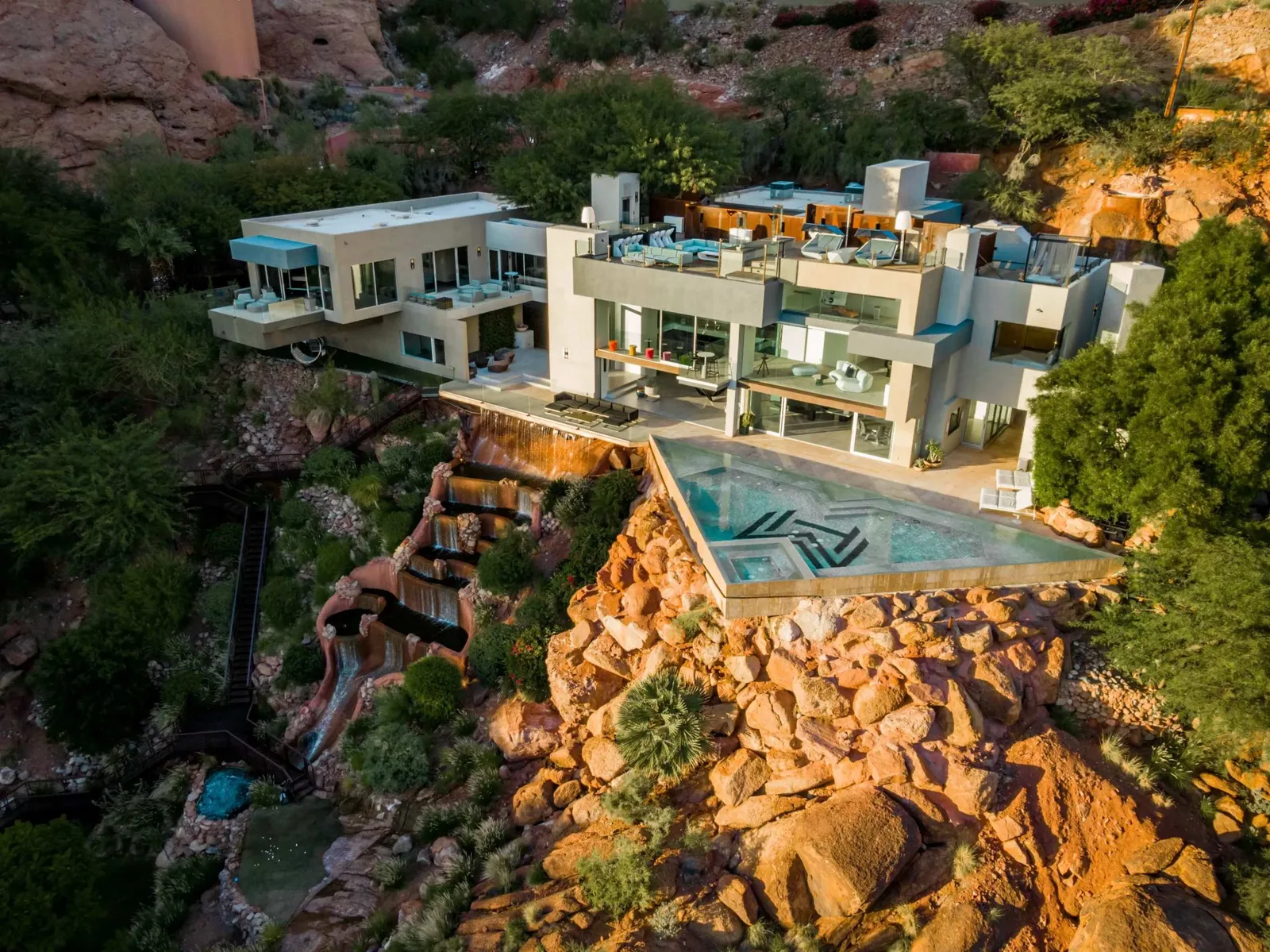Modern desert home built into red-rock cliffs with an infinity pool and cascading water features near Scottsdale, Arizona, at golden hour