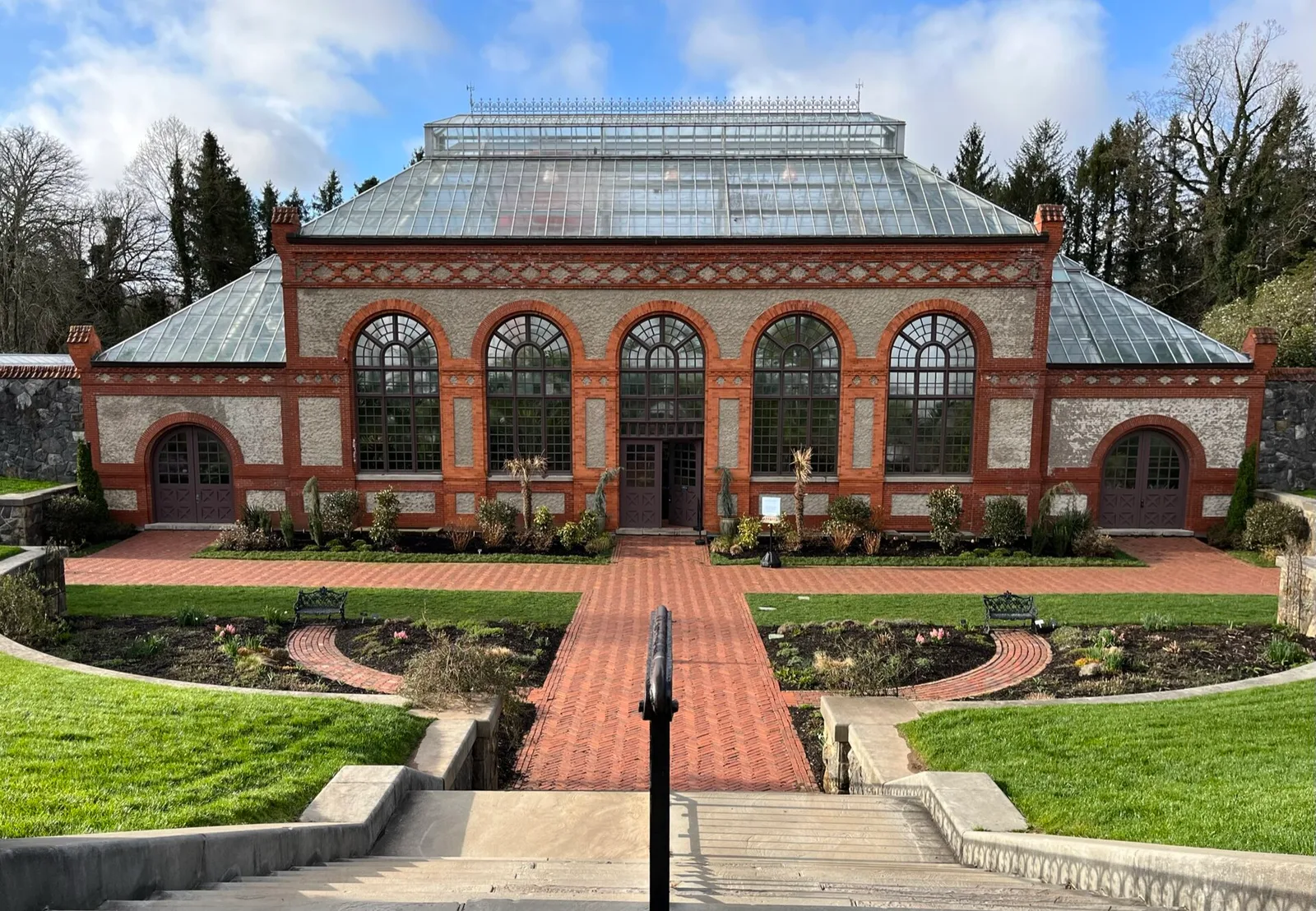 The brick and glass conservatory of the Biltmore Estate above a manicured walled garden under a blue sky in Asheville, North Carolina