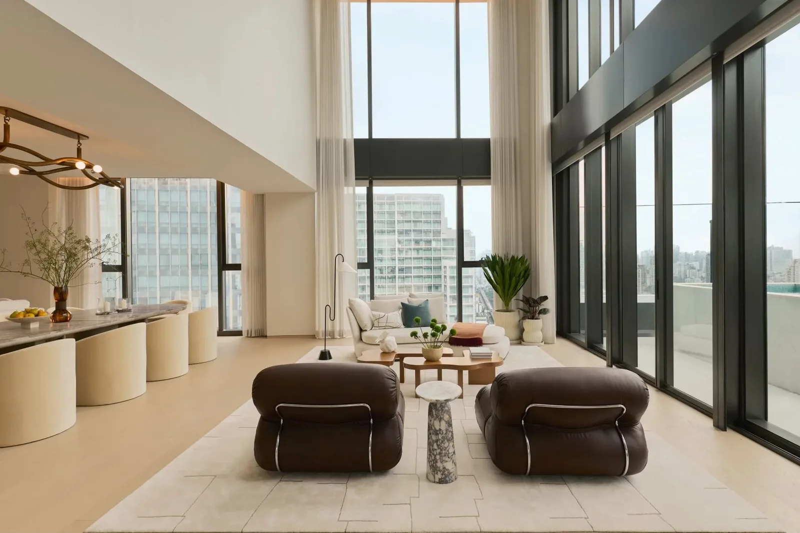 Double-height luxury penthouse living room with floor-to-ceiling windows overlooking a dense high-rise city skyline in Bangkok, Thailand